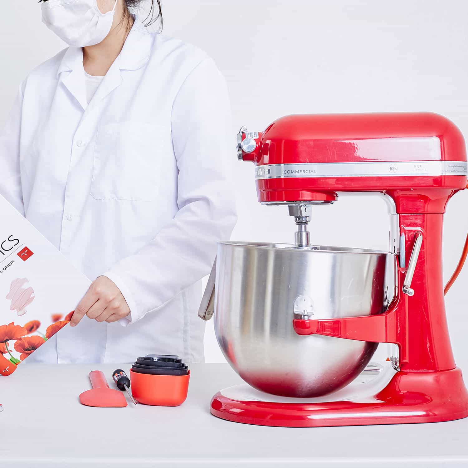 mujer con tapabocas leyendo libro junto a maquina mezcladora roja